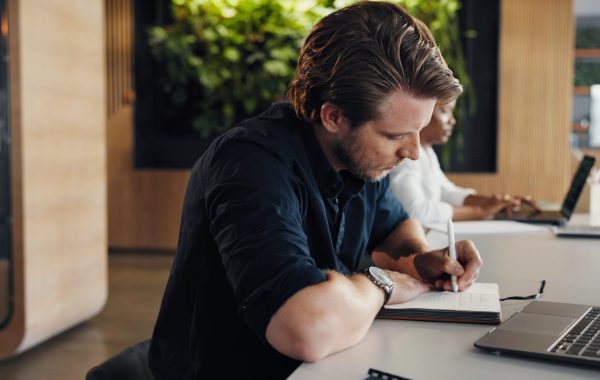Design, laptop and writing with business man in coworking office for development or planning. Computer, notebook and research with designer person at desk in workplace for agenda or schedule.